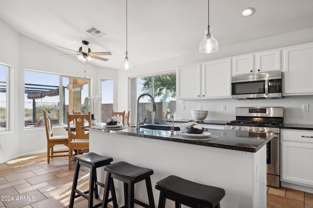 kitchen featuring stainless steel appliances, a sink, an island with sink, a ceiling fan, and white cabinetry