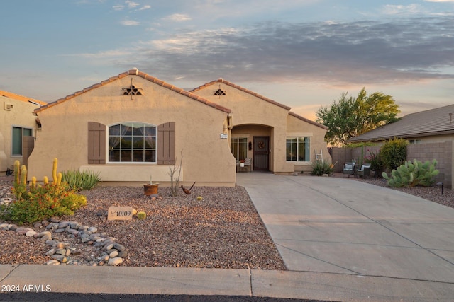 mediterranean / spanish house with stucco siding, a tiled roof, driveway, and fence