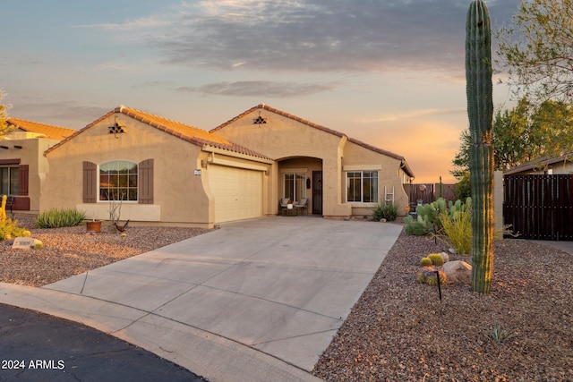 mediterranean / spanish-style house with stucco siding, fence, concrete driveway, a tiled roof, and an attached garage