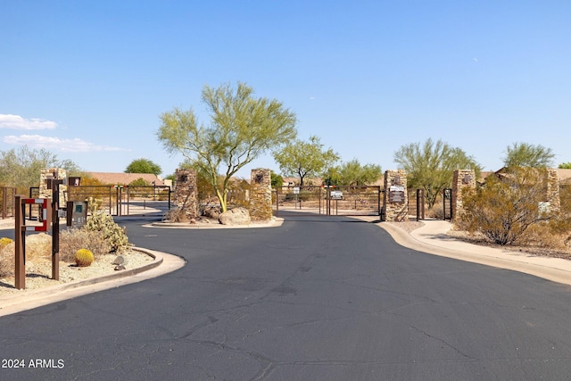 view of asphalt road featuring a gate, a gated entry, and curbs