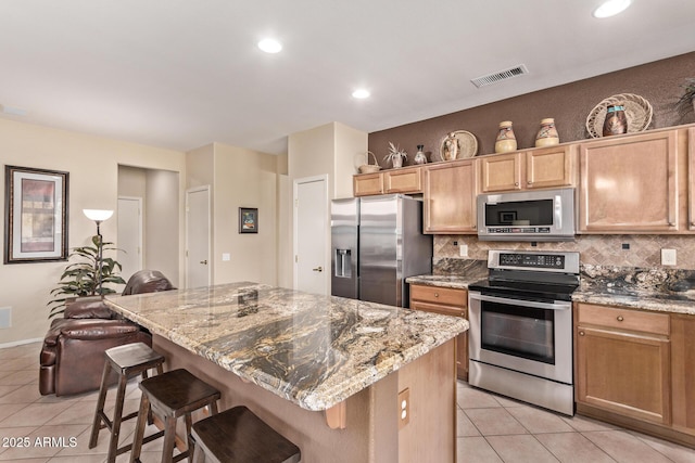 kitchen with a kitchen bar, light stone countertops, a center island, and appliances with stainless steel finishes