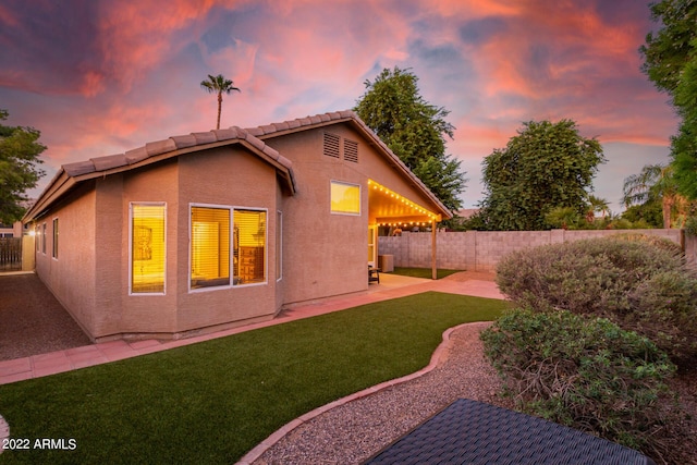 back house at dusk with a patio and a lawn