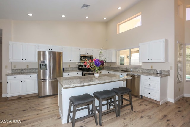 kitchen featuring white cabinetry, a towering ceiling, appliances with stainless steel finishes, and a sink