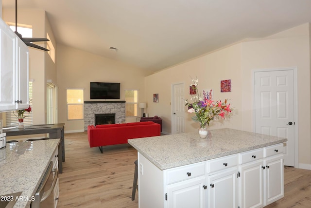 kitchen with light wood-type flooring, light stone counters, a stone fireplace, white cabinets, and vaulted ceiling