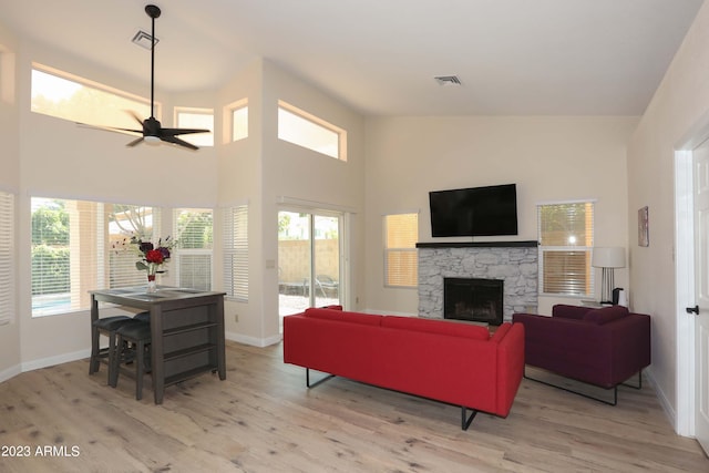 living area featuring wood finished floors, a stone fireplace, ceiling fan, and a healthy amount of sunlight