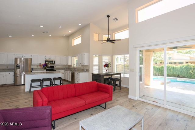 living room with visible vents, light wood-style flooring, recessed lighting, ceiling fan, and a towering ceiling