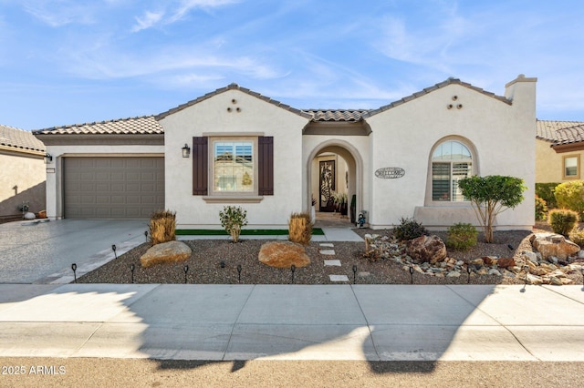 mediterranean / spanish house with a garage, driveway, a tiled roof, and stucco siding