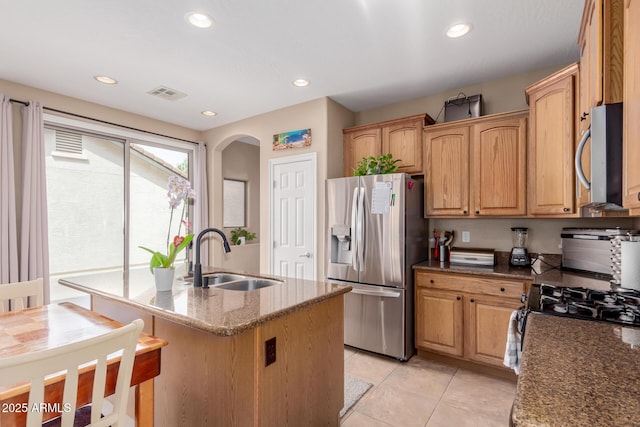 kitchen featuring visible vents, dark stone counters, stainless steel appliances, arched walkways, and a sink