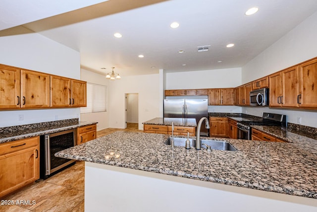 kitchen featuring a sink, appliances with stainless steel finishes, beverage cooler, dark stone countertops, and visible vents