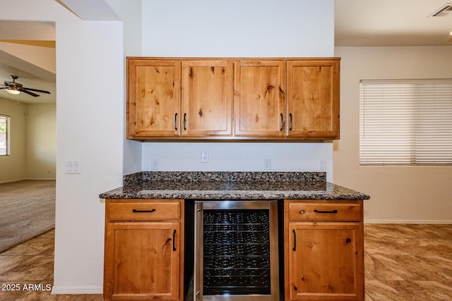 kitchen with visible vents, brown cabinets, dark stone counters, wine cooler, and a ceiling fan