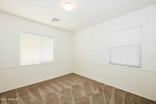 carpeted spare room with visible vents and wainscoting