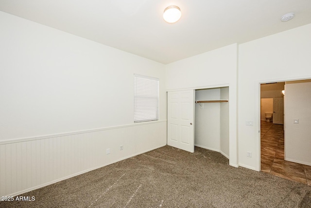 unfurnished bedroom featuring a closet, carpet flooring, and a wainscoted wall
