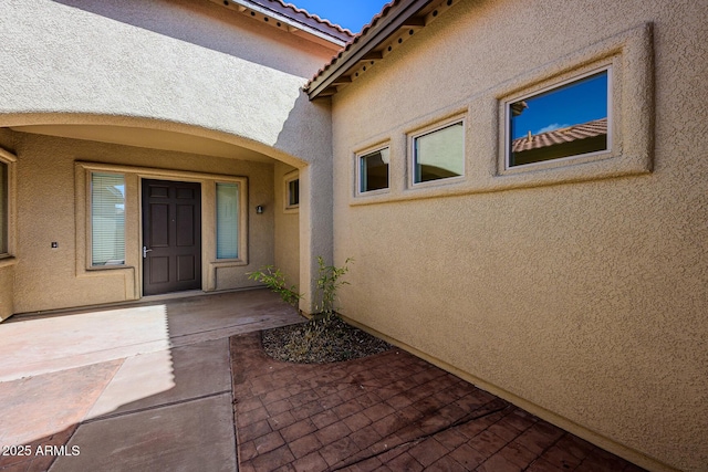 entrance to property with stucco siding, a tile roof, and a patio area