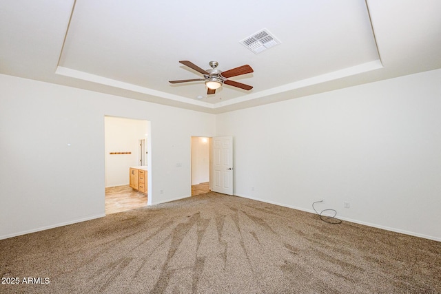 unfurnished bedroom with a raised ceiling, light carpet, ensuite bathroom, baseboards, and visible vents