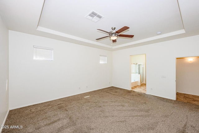 carpeted spare room with a tray ceiling, baseboards, visible vents, and a ceiling fan