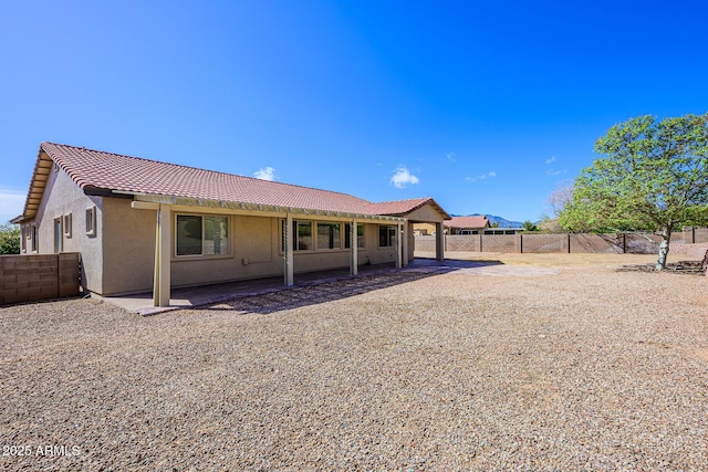 rear view of property with a fenced backyard, stucco siding, a tiled roof, and a patio
