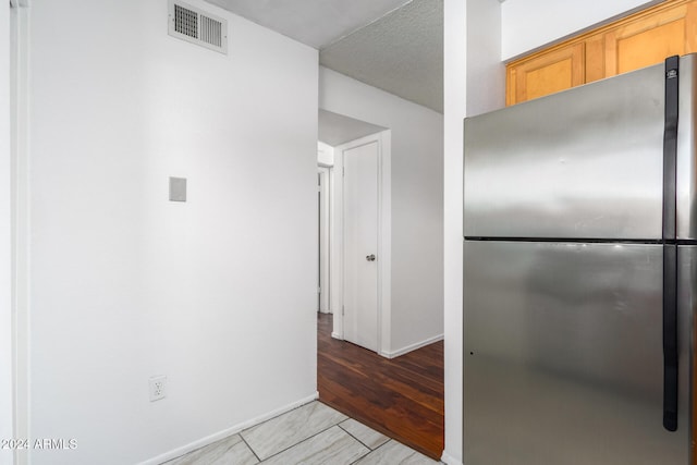 kitchen featuring a textured ceiling, light brown cabinetry, and stainless steel refrigerator