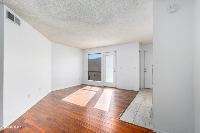 unfurnished room with hardwood / wood-style flooring and a textured ceiling