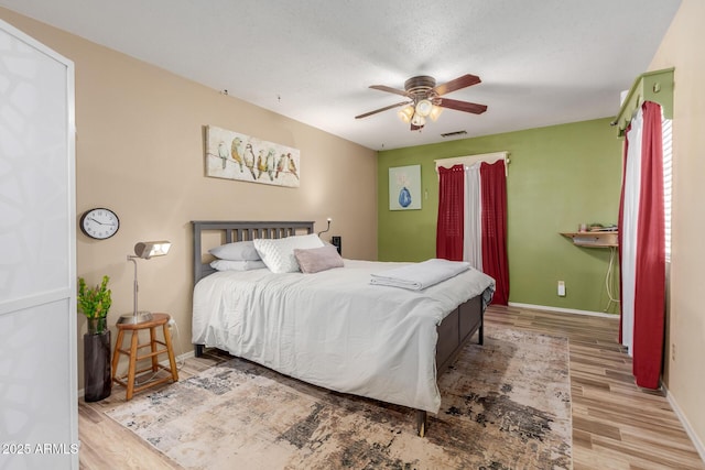 bedroom with baseboards, visible vents, ceiling fan, wood finished floors, and a textured ceiling