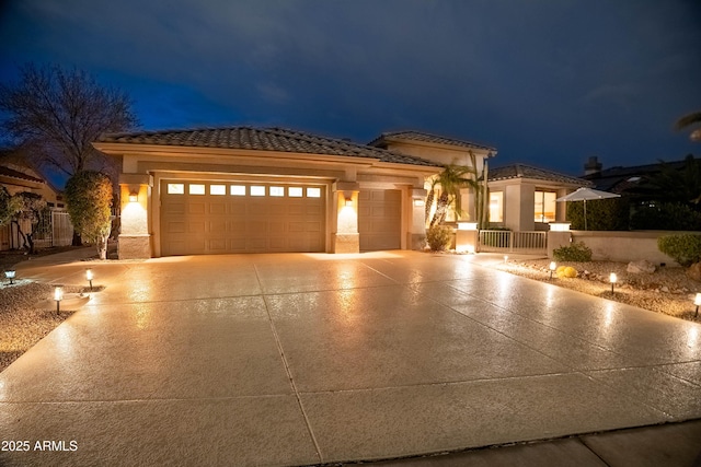 view of front of home featuring fence, a tiled roof, concrete driveway, stucco siding, and a garage