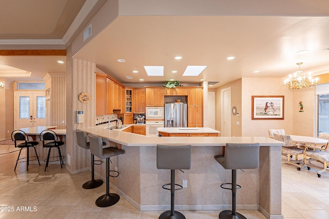 kitchen with visible vents, a sink, a kitchen breakfast bar, white appliances, and a peninsula