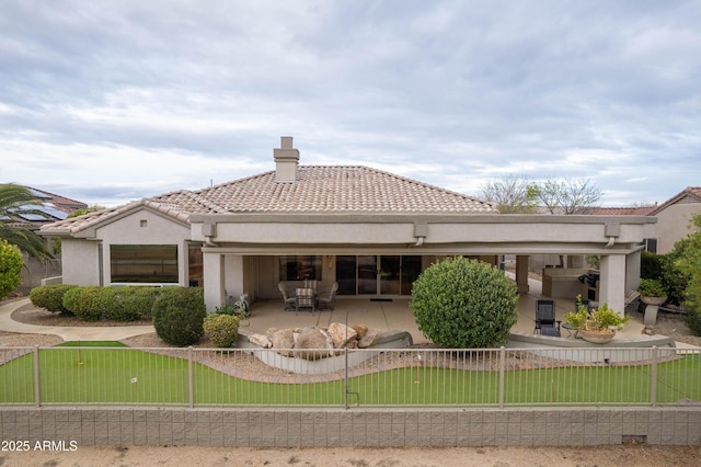 back of property with stucco siding, a tiled roof, a chimney, and a patio