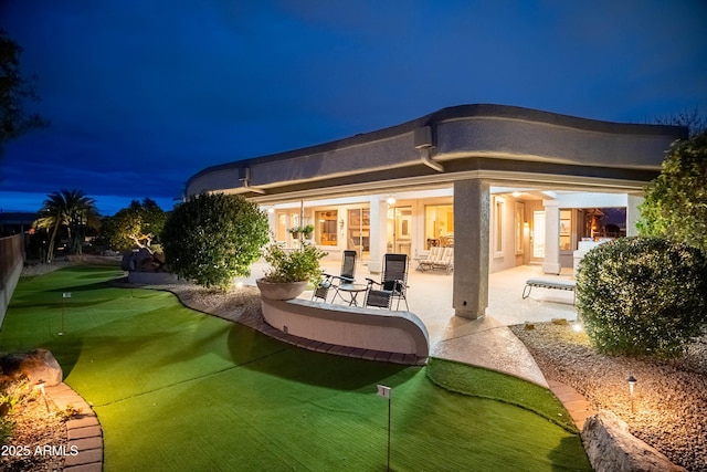 back of house at night with a patio and stucco siding