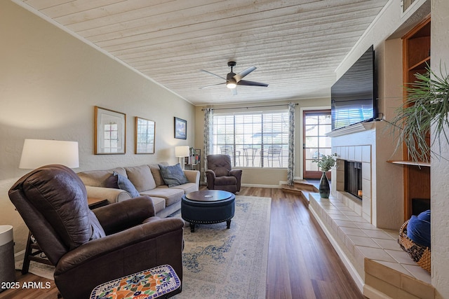 living room featuring wood ceiling, a tiled fireplace, light wood-type flooring, crown molding, and ceiling fan