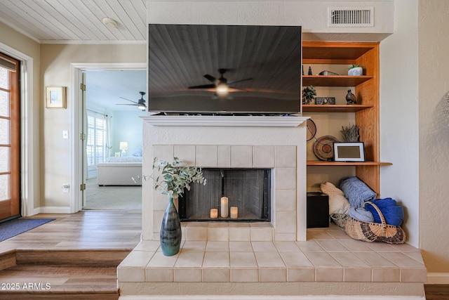 living room with wood-type flooring, a tiled fireplace, ceiling fan, and built in features