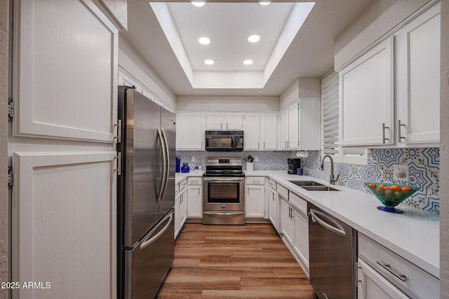 kitchen featuring stainless steel appliances, sink, white cabinetry, a raised ceiling, and light hardwood / wood-style flooring