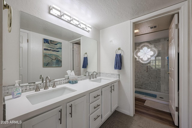 bathroom with a tile shower, wood-type flooring, vanity, and a textured ceiling