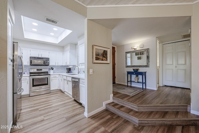 kitchen featuring stainless steel appliances, decorative backsplash, white cabinets, light hardwood / wood-style flooring, and sink