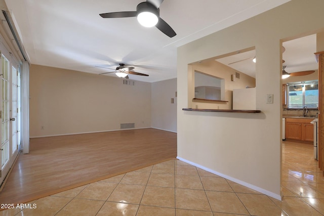 unfurnished living room with light tile patterned floors, ceiling fan, crown molding, and sink