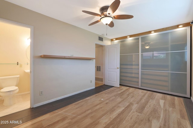 unfurnished bedroom featuring a closet, ensuite bath, ceiling fan, and hardwood / wood-style floors