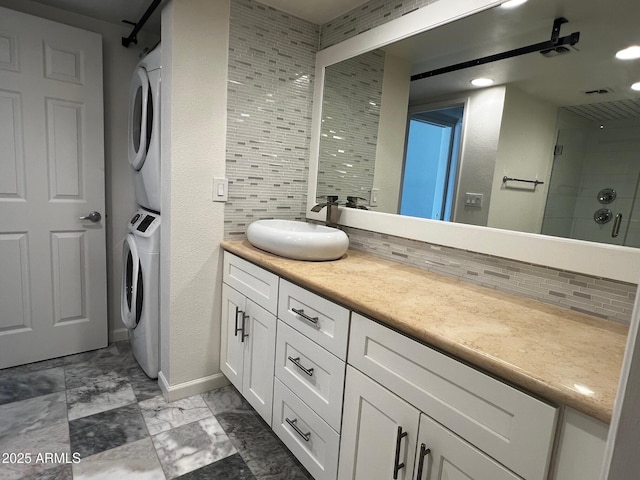bathroom featuring a stall shower, baseboards, decorative backsplash, stacked washer / drying machine, and vanity
