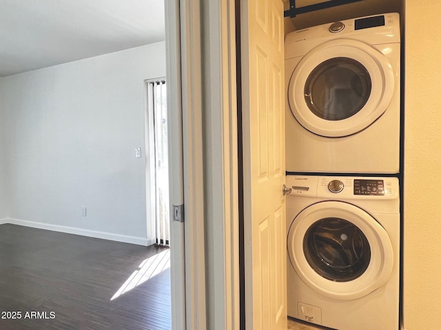 washroom featuring baseboards, wood finished floors, stacked washer and dryer, and laundry area