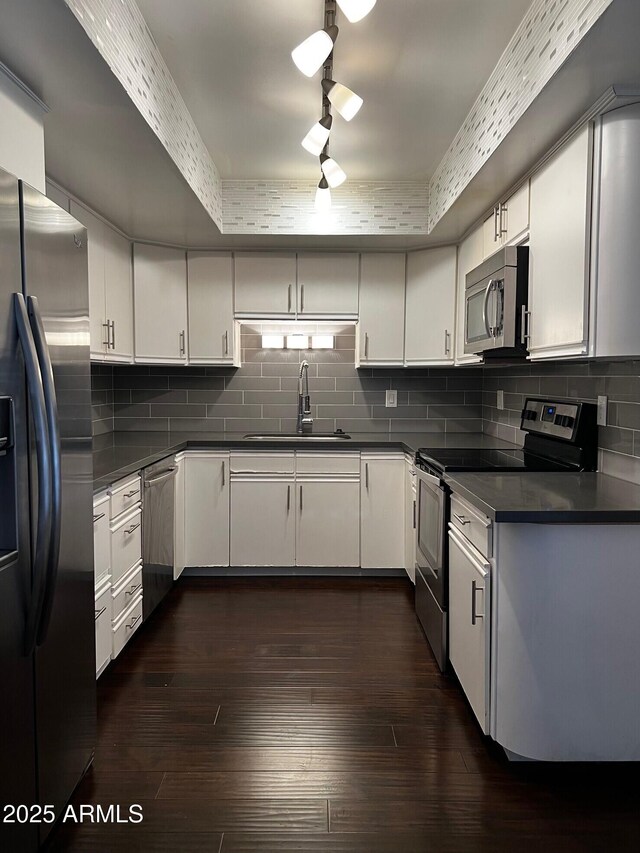 kitchen with a sink, dark wood-style flooring, dark countertops, backsplash, and appliances with stainless steel finishes