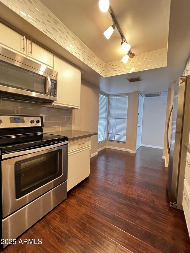 kitchen with rail lighting, appliances with stainless steel finishes, white cabinetry, backsplash, and dark wood-style flooring