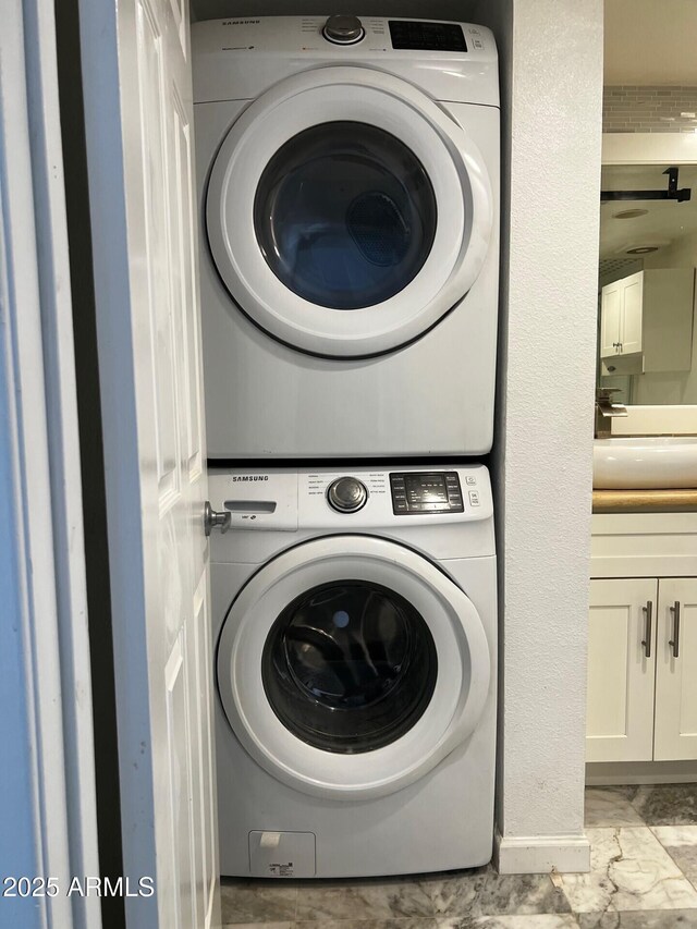 laundry room with stacked washer and dryer, marble finish floor, a sink, and laundry area