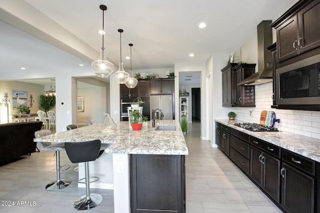 kitchen with a large island, wall chimney range hood, stainless steel appliances, and sink