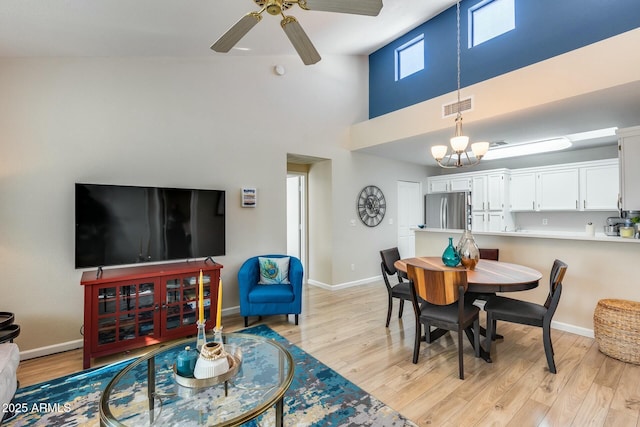 dining space with ceiling fan with notable chandelier, light hardwood / wood-style flooring, and a high ceiling