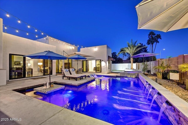 pool at night with a patio area, a fenced in pool, and a fenced backyard