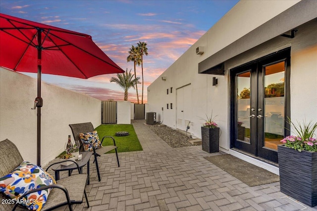 patio terrace at dusk featuring cooling unit, french doors, and fence