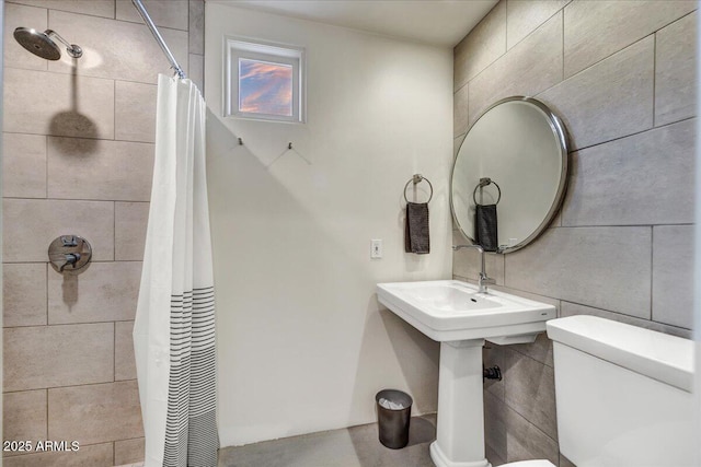 bathroom featuring tiled shower, toilet, and tile walls