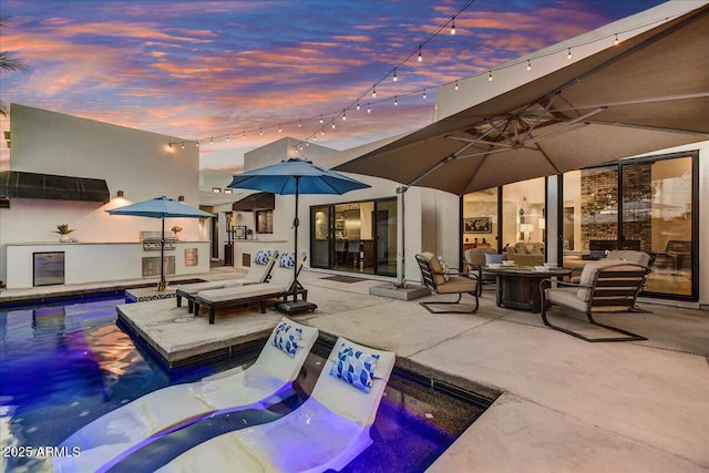 pool at dusk with a patio area, an outdoor pool, outdoor lounge area, and exterior kitchen