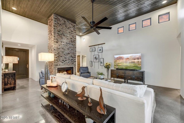 living area with a brick fireplace, concrete floors, recessed lighting, wooden ceiling, and a high ceiling