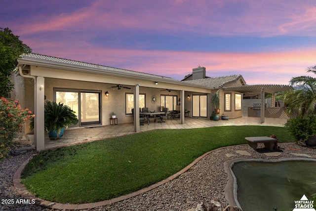 3394 N 147th Ln, Goodyear, AZ 85395 - back of property at dusk featuring ceiling fan, a pergola, a chimney, a lawn, and stucco siding
