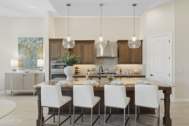 6450 E Monterra Way, Scottsdale, AZ 85266 - kitchen featuring wall chimney range hood, double oven, backsplash, light tile patterned floors, and a breakfast bar