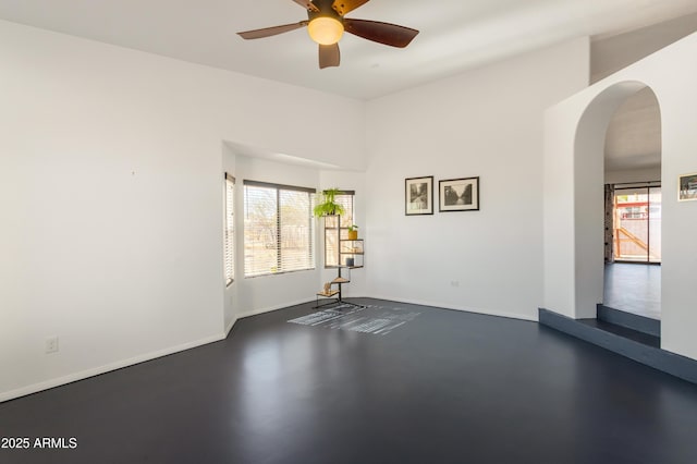empty room featuring arched walkways, ceiling fan, baseboards, and plenty of natural light