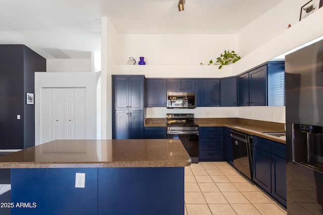 kitchen featuring light tile patterned floors, blue cabinetry, a kitchen island, dark stone counters, and appliances with stainless steel finishes